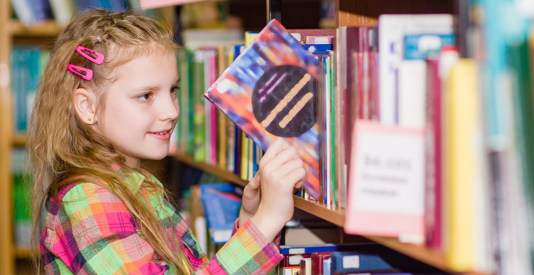 Jeune fille qui choisit un livre en Français dans la bibliothèque de l'école